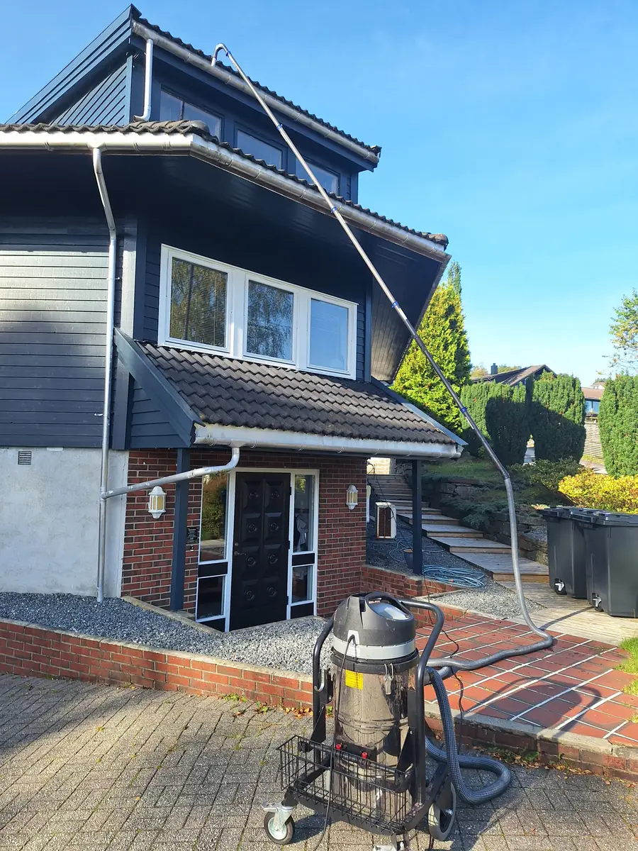 SkyVac Nitro med lang stang opp til takrennen på et mørkt trehus
